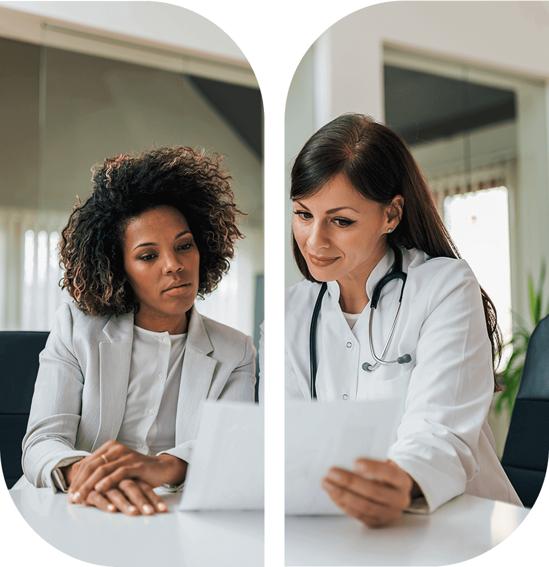 Two women sitting at a table. One is in business attire, the other in a white coat with a stethoscope. They are reviewing documents together in an office setting.